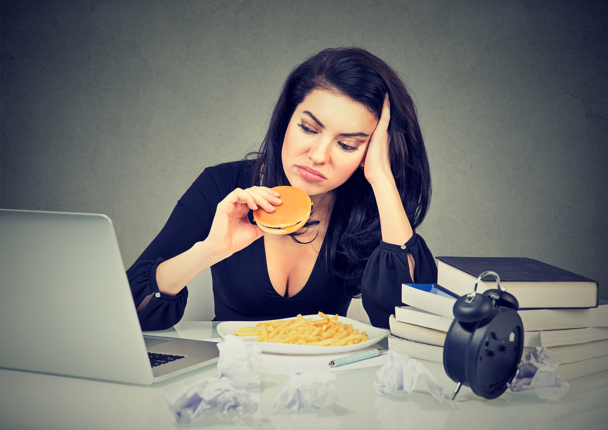 Sedentary lifestyle and junk food concept. Tired stressed woman sitting at her desk eating hamburger and french fries
