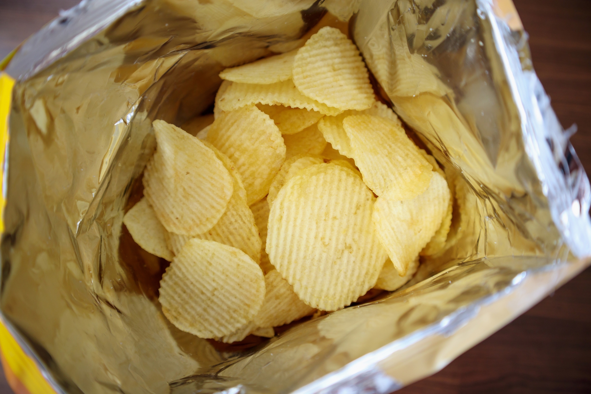 Potato chips in open snack bag close up on table floor