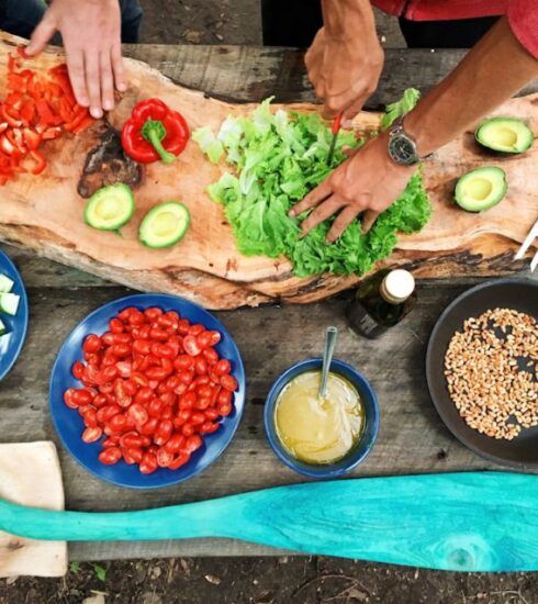 Cooking - person slicing green vegetable in front of round ceramic plates with assorted sliced vegetables during daytime