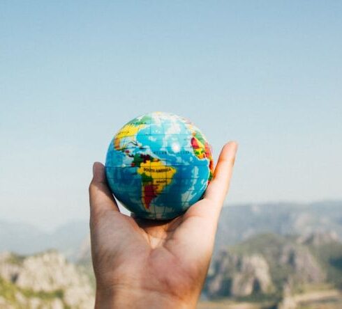 Traveling - Person Holding World Globe Facing Mountain