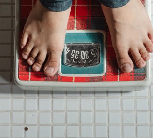 Weight Loss - From above crop anonymous barefoot child in jeans standing on weigh scales on tiled floor of bathroom