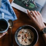 Diet - Person Holding White Ceramic Coffee Cup Leaning on Brown Wooden Table