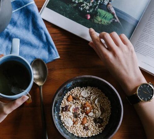 Diet - Person Holding White Ceramic Coffee Cup Leaning on Brown Wooden Table