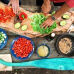 Cooking - person slicing green vegetable in front of round ceramic plates with assorted sliced vegetables during daytime