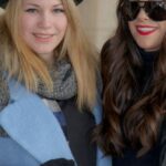 Coats - Chic Duo: Two Women in Coordinating Blue Coats, Black Hats, and Striking Red Handbags Strike a Pose