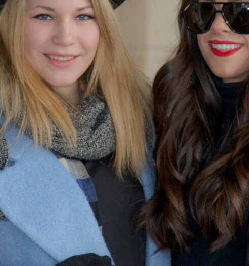 Coats - Chic Duo: Two Women in Coordinating Blue Coats, Black Hats, and Striking Red Handbags Strike a Pose