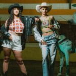 Tops - Two women in cowboy hats standing next to horses