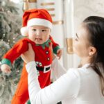 Rompers - A woman holding a baby in front of a christmas tree