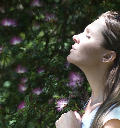 Breathing - Woman Closing Her Eyes Against Sun Light Standing Near Purple Petaled Flower Plant