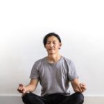 Mindfulness - Photo of Man in Gray T-shirt and Black Jeans on Sitting on Wooden Floor Meditating