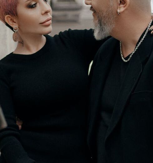 Communication - Elegant short haired woman in black dress embracing stylish bald middle aged man while standing together near old stone building in city