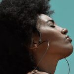 Mindfulness - From below side view of young reflective ethnic female model with big earrings and closed eyes under blue sky