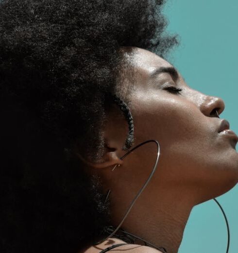 Mindfulness - From below side view of young reflective ethnic female model with big earrings and closed eyes under blue sky