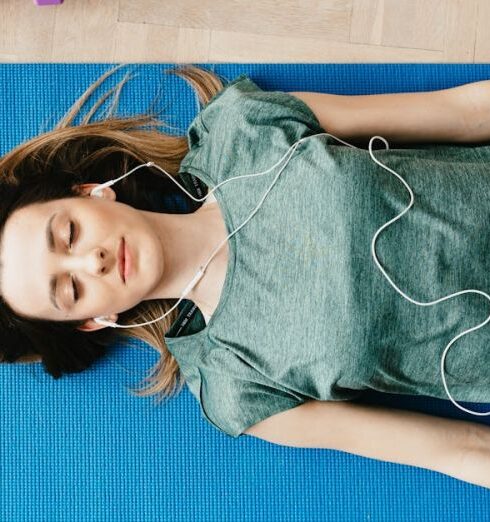 Mindfulness - Peaceful woman in earphones resting in Shavasana pose at home