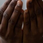 Mindfulness - Selective focus of crop anonymous African American man wearing white turtleneck praying with open hands