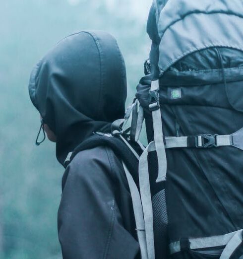 Backpacking - Man Wearing Black Hoodie Carries Black and Gray Backpacker Near Trees during Foggy Weather