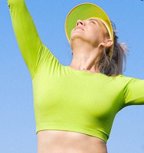 Training - From below of sportive woman in tennis cap wearing green top serving ball and looking up while standing on court with raised arm and rocket in hand