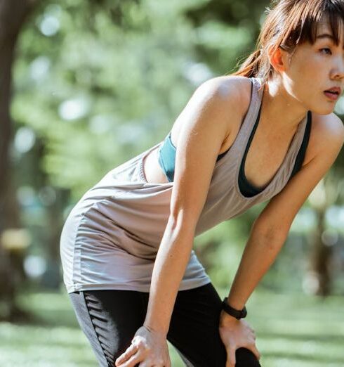 Recovery - Tired ethnic female in sportswear looking away while leaning on knees having rest after workout in park on sunny summer day