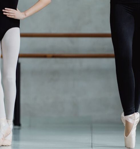 Training - Crop unrecognizable ballerinas in leotards standing on tiptoes with hands on waist while practicing dance movements in light studio