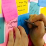 Improvement - Person Writing on Pink Sticky Notes