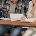 Issues - A Couple Sitting Near the Wooden Table while Looking at the Document in Shocked Emotion