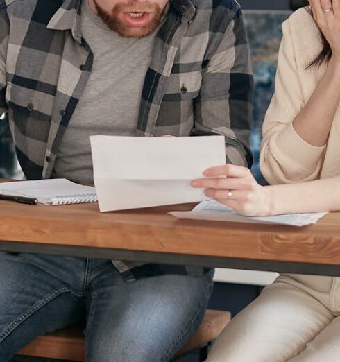 Issues - A Couple Sitting Near the Wooden Table while Looking at the Document in Shocked Emotion