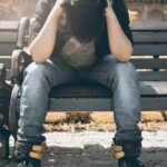 Stress - Man in Black Shirt and Gray Denim Pants Sitting on Gray Padded Bench