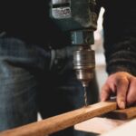 Woodworking - Man Holding Wooden Stick While Drilling Hole