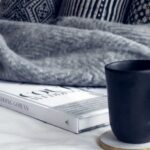 Blanket - Black Ceramic Mug on Round White and Beige Coaster on White Textile Beside Book