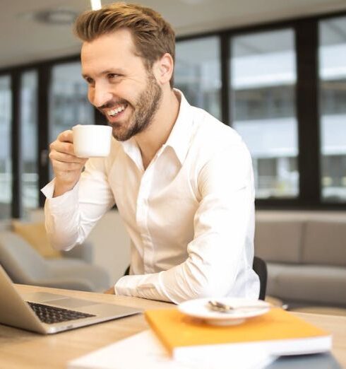 Work - Depth of Field Photo of Man Sitting on Chair While Holding Cup in Front of Table