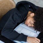 Overload - High angle of exhausted African American student resting on opened textbook and papers while preparing for exam