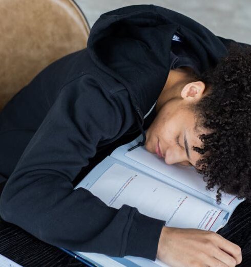 Overload - High angle of exhausted African American student resting on opened textbook and papers while preparing for exam