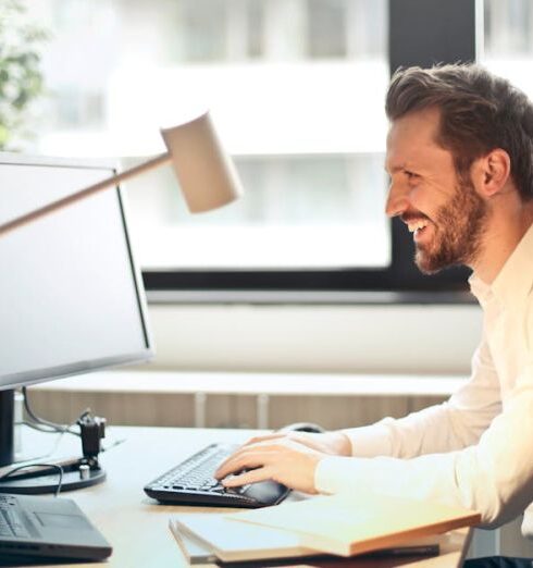 Emails - Man in White Dress Shirt Sitting on Black Rolling Chair While Facing Black Computer Set and Smiling