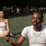 Mindfulness - Full body of flexible barefoot couple in activewear sitting on mats in Lotus pose with closed eyes while practicing yoga together