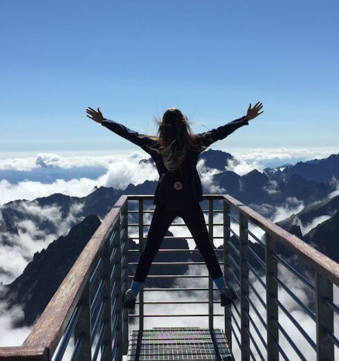 Success - Person Standing on Hand Rails With Arms Wide Open Facing the Mountains and Clouds