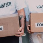 Volunteering - Man and Woman Carrying Medicine and Food Labelled Cardboard Boxes Behind a White Van