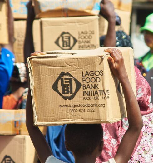 Food Bank - People Walking and Carrying Boxed on Their Heads