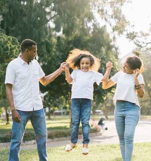 Family - A Man and a Woman Assisting a Girl While Jumping