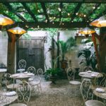 Pergola - Cafe with setting on ornamental tables near chairs under decorative lamps in backyard on summer day