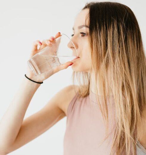 Drink Water - Young thirsty fit female with long hair in sportswear drinking water while recreating after workout