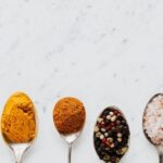 Cooking - Top view of assorted aromatic condiments arranged together in metal spoons on marble surface used for delicious gourmet meal cooking