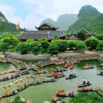 Boat Festival - Aerial Photography of Building Surrounded With Body of Water With Boats Across Tree Covered Hills