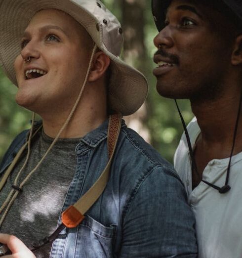 Surprise Trip - Side view astonished diverse males in casual summer clothes standing with photo camera in verdant forest and looking up in surprise