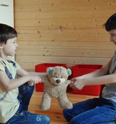 Sibling Arguments - Side view full length irritated fighting brothers sitting on floor and pulling teddy bear to sides