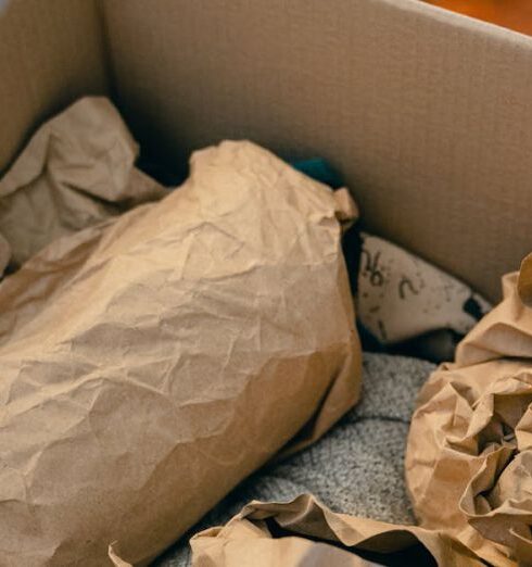 Packing - From above of open cardboard box on wooden floor full of things wrapped in packaging paper prepared for moving in new apartment