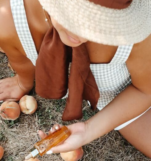 Sunburn - From above of unrecognizable tanned female wearing casual clothes with straw hat sitting on dry grass near woven bag and scattered peaches