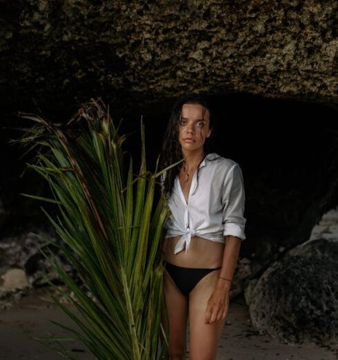 Hidden Beaches - Sad woman in bikini standing with palm branch in cave