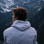 Solo - A Man in White Hoodie Sitting on a Rock Across the Mountains