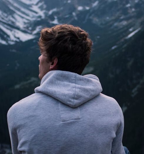 Solo - A Man in White Hoodie Sitting on a Rock Across the Mountains