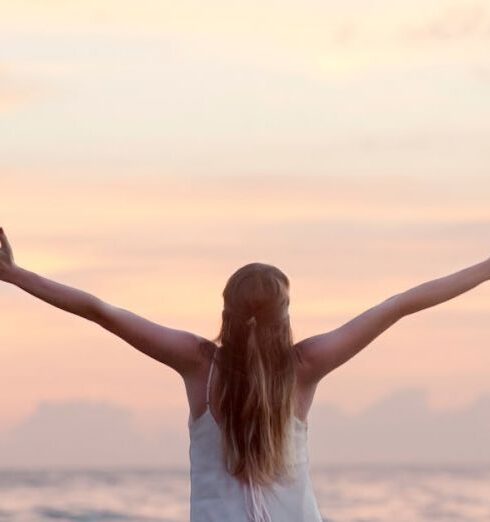 Healthy - Rear View of Woman With Arms Raised at Beach during Sunset